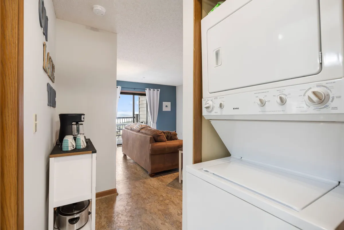 This image captures a practical laundry nook featuring a stackable washer and dryer, adjacent to a coffee station and living area. The setup illustrates convenience and efficient use of space for guests needing to refresh their wardrobe after outdoor adventures.
