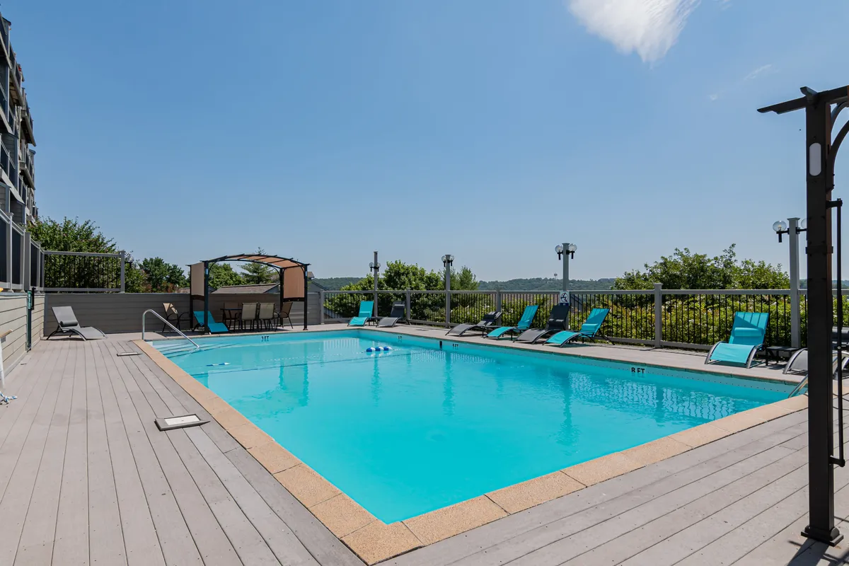 A vibrant outdoor swimming pool area with lounge chairs and a canopy, surrounded by greenery. The space is clearly designed for relaxation, sunbathing, and family gatherings, capturing the essence of summertime fun at the resort.