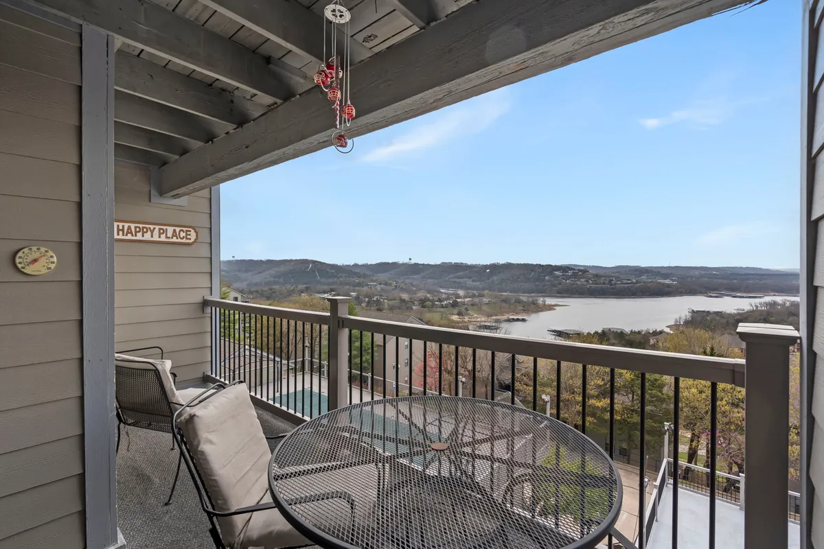 This exterior photo presents a peaceful lake view from a balcony furnished with comfortable seating and a decorative 'HAPPY PLACE' sign. The image captures the opportunity for guests to enjoy lake access, scenic vistas, and moments of relaxation right outside the condo.