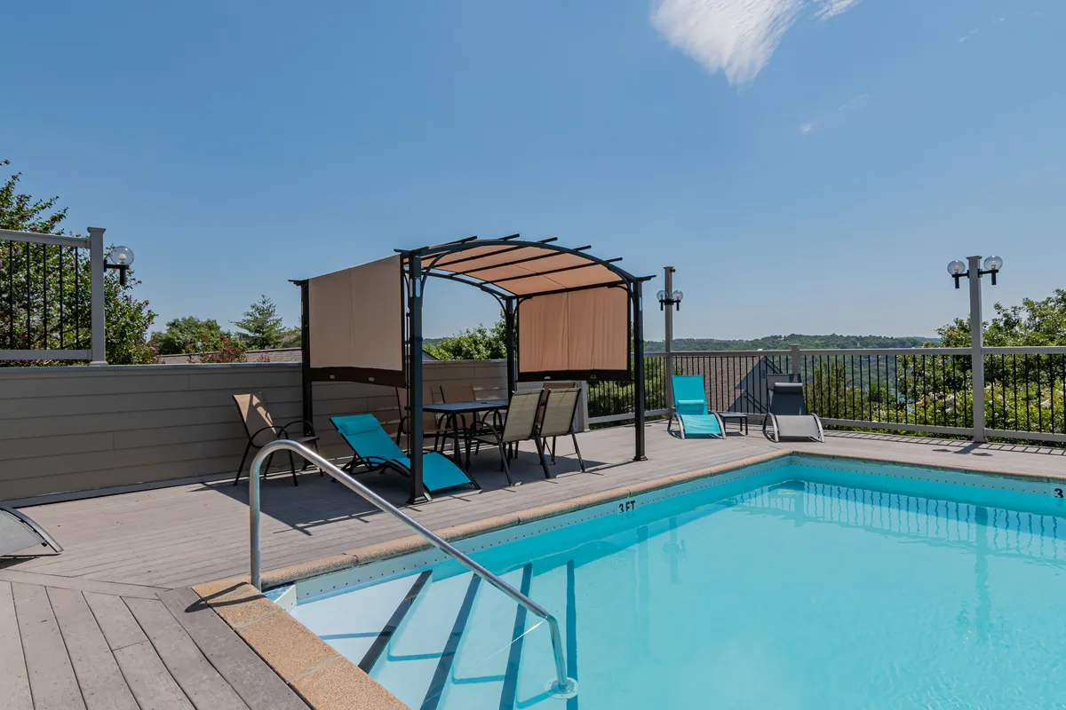 This exterior image showcases the resort's swimming pool surrounded by lounge chairs, a canopy seating area, and lush greenery. The tranquil atmosphere is enhanced by the inviting water and comfortable spaces for sunbathing or socializing, perfectly representing the seasonal outdoor pool amenity.