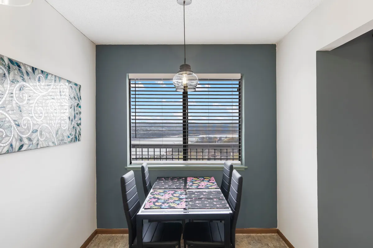 A welcoming dining area with a spacious table, complemented by artwork on the wall and a bright window that frames serene outdoor scenery. The atmosphere suggests a setting ideal for meals, laughter, and casual gatherings, with natural light enhancing the inviting mood.