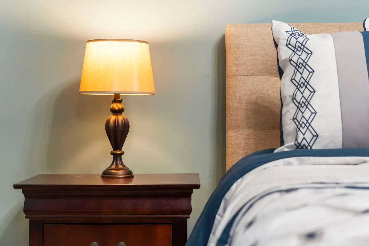 A tranquil bedroom scene with a bed adorned in soft bedding, a nightstand, and a gentle lamp glow creating a peaceful atmosphere. The focus is on the inviting, restful nature of the space, with calming colors and an uncluttered feel.