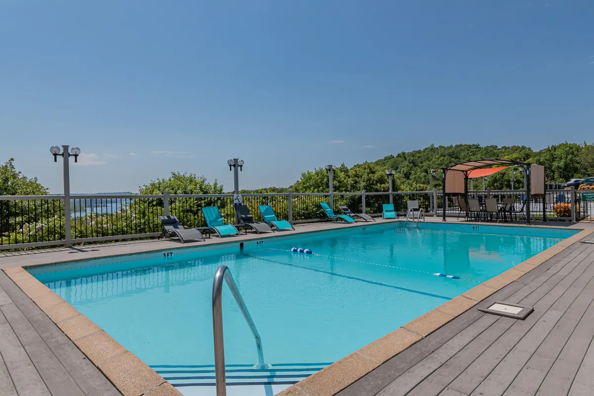 A serene swimming pool area with lounge chairs overlooks a scenic landscaped view, setting a tranquil mood. The poolside setting offers opportunities for relaxation, sunbathing, and soaking up the outdoors, all in a peaceful lakeside environment.