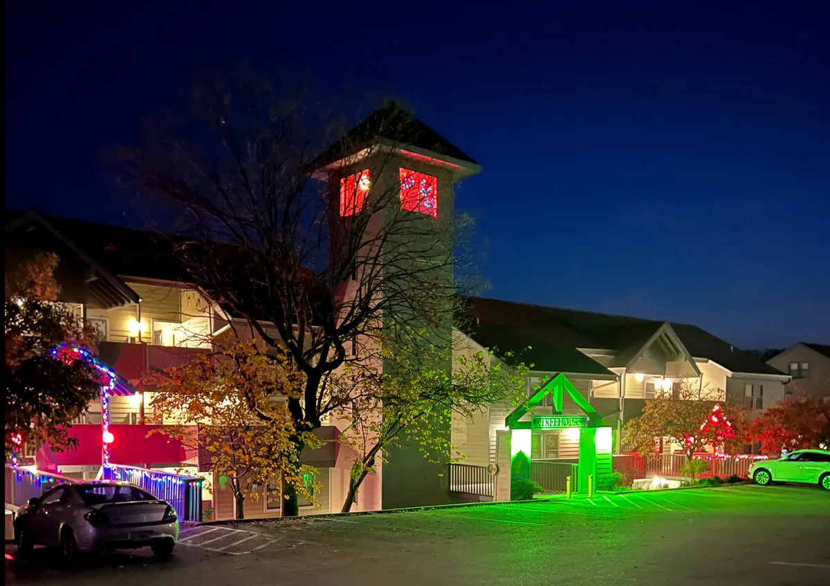 The property’s exterior comes alive at night with decorative lighting, an illuminated tower, a green entrance sign, and colorful trees. The scene feels welcoming and festive—perfect for capturing the magic of Branson nights.