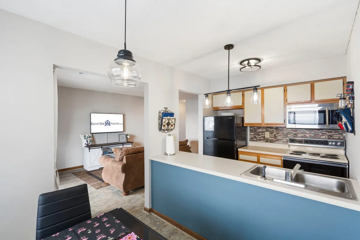 A spacious, modern interior shows a kitchen, living room, dining table, and television in an open plan, all designed for casual comfort. The space is well-lit and inviting, suggesting relaxing evenings and easy living for guests.