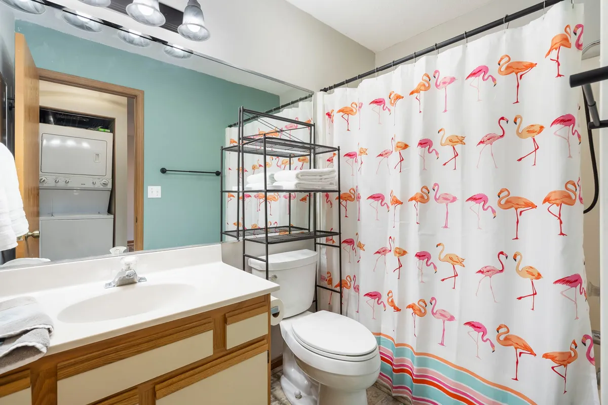 A modern bathroom featuring a clean white vanity, a cheerful flamingo shower curtain, and a practical storage rack. The space feels fresh, bright, and family-friendly, highlighting both function and a touch of fun.